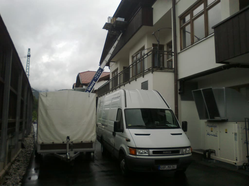 Transporter mit Anhänger vor einem Wohnhaus, daneben ein ausgefahrener Möbellift